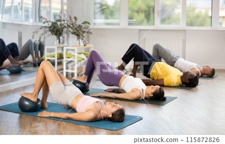 Woman performing glute bridge with ball during group pilates class 115872826