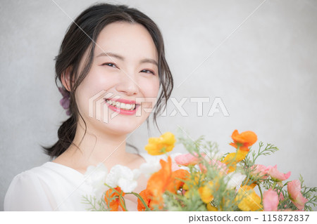 Cosmetic and beauty portrait of a young woman holding a bouquet of flowers, orange and pink image, looking at camera 115872837