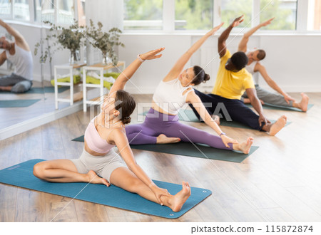 Young girl performing arivrtta Janu Sirsasana in yoga class Young girl performing arivrtta Janu Sirsasana in yoga class 115872874