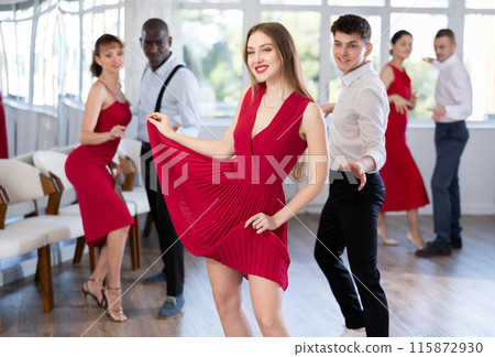 Happy young Woman in red dress with man practising charleston dancing in dance hall 115872930