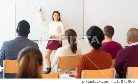 Group of students attentively listening to lecture of female teacher Group of students attentively listening to lecture of female teacher 115873069