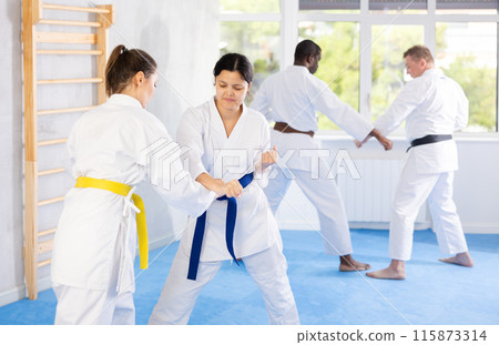 Middle-aged woman attendee of karate classes fighting with her opponent in sports hall Middle-aged woman attendee of karate classes fighting with her opponent in sports hall 115873314
