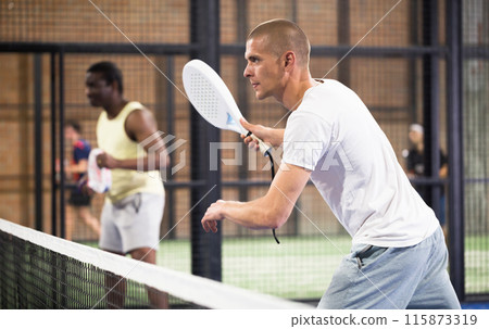 Focused man playing paddle ball match on closed court 115873319
