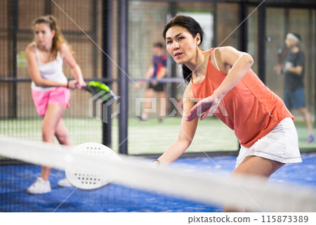 Four smiling men and women with padel rackets posing at court 115873389