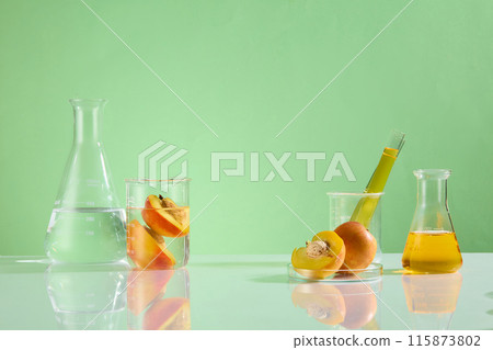 An erlenmeyer with yellow liquid displayed on the right of white table, beside a beaker, test tube and petri dish containing fresh peaches. A transparent liquid flask and a beaker placed on the left An erlenmeyer with yellow liquid displayed on the right of white table, beside a beaker, test tube and petri dish containing fresh peaches. A transparent liquid flask and a beaker placed on the left 115873802
