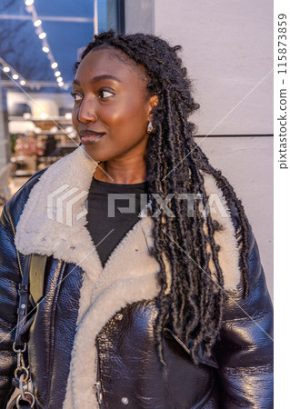 A trendy woman wrapped in a cozy coat gazes contemplatively at the city lights on a winter evening 115873859