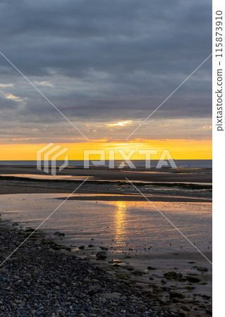 Witness the beauty of a stunning sunset over the beach, with reflective water and a dramatic sky 115873910