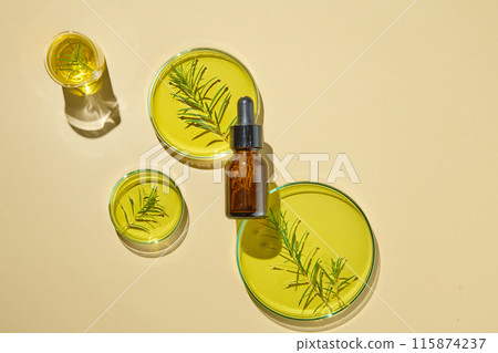 Beige background features a beaker, three petri dishes and a serum bottle without label. Glassware filled with oil and tea tree leaves. Natural beauty blank label for branding mock-up concept 115874237