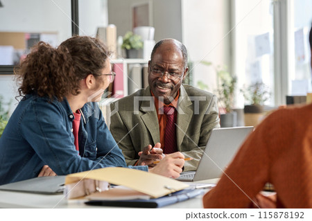 Portrait of smiling senior man talking to young colleague in business meeting and enjoying work in age inclusive office copy space 115878192