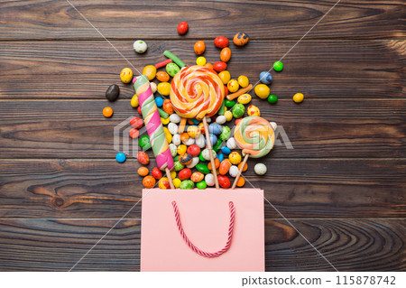 shopping paper gift bag in corner full of assorted traditional candies falling out on colored background with copy space. Happy Holidays sale concept shopping paper gift bag in corner full of assorted traditional candies falling out on colored background with copy space. Happy Holidays sale concept 115878742