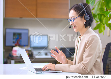A middle-aged woman wearing a headset working in an office A middle-aged woman wearing a headset working in an office 115878869