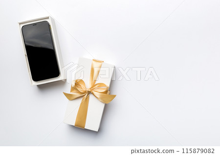 Opened gift box with gold ribbon and smartphone on color background, top view. Blank open box packaging mockup , Template for your design - branding mockup Opened gift box with gold ribbon and smartphone on color background, top view. Blank open box packaging mockup , Template for your design - branding mockup 115879082