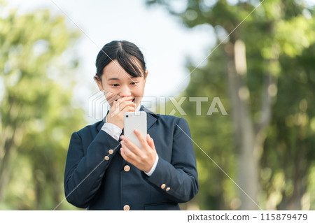穿著制服和西裝外套的國中女生和高中女生看著自己的智慧型手機時感到驚訝、高興、驚訝。 115879479