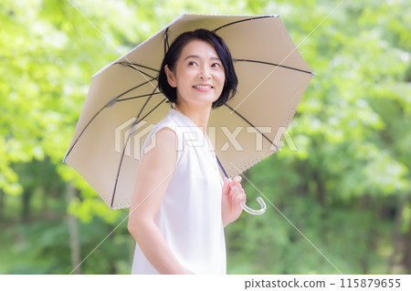 A middle-aged woman walking with a parasol among the fresh greenery A middle-aged woman walking with a parasol among the fresh greenery 115879655