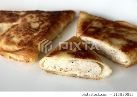 Fried triangle pancakes with chicken meat lie on a white plate Fried triangle pancakes with chicken meat lie on a white plate 115880835