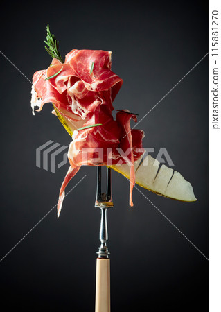 Melon with prosciutto and rosemary on a black background. Melon with prosciutto and rosemary on a black background. 115881270