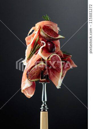 Prosciutto with figs, rosemary, and red olives on a fork. 115881272