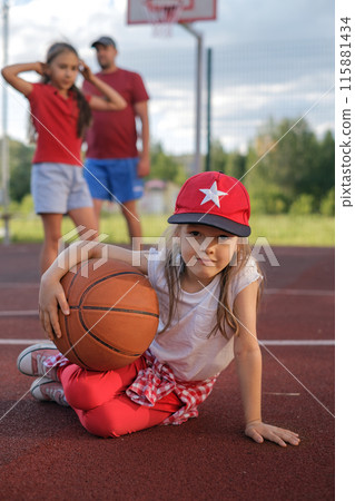 A cute little girl in a baseball cap sits with a basketball on the playground after a game A cute little girl in a baseball cap sits with a basketball on the playground after a game 115881434