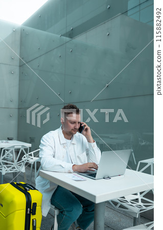 Young Caucasian male passenger in stylish casual clothes using smartphone and laptop keyboard, sit has training online meeting on laptop computer in airline lounge wait transit international airport Young Caucasian male passenger in stylish casual clothes using smartphone and laptop keyboard, sit has training online meeting on laptop computer in airline lounge wait transit international airport 115882492