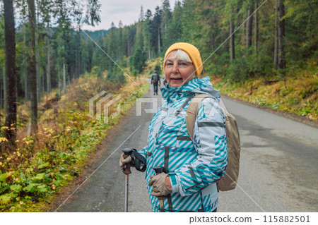 Mature caucasian blonde woman on vacation, having a hike in autumn mountains with backpack and hiking poles, enjoying adventure. 115882501