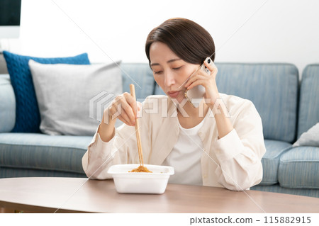 A woman in her 40s eating yakisoba while talking on the phone 115882915
