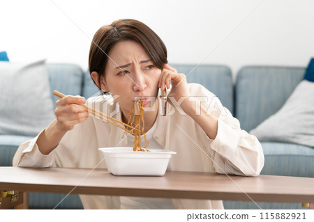 A woman in her 40s eating yakisoba while talking on the phone A woman in her 40s eating yakisoba while talking on the phone 115882921