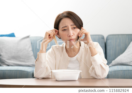 A woman in her 40s eating yakisoba while talking on the phone A woman in her 40s eating yakisoba while talking on the phone 115882924
