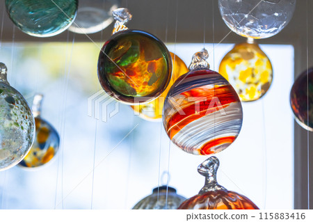 Colorful transparent glass balls hang in front of bright window, close up 115883416