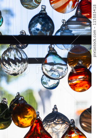 Colorful glass balls hang in front of bright window, vertical photo Colorful glass balls hang in front of bright window, vertical photo 115883418
