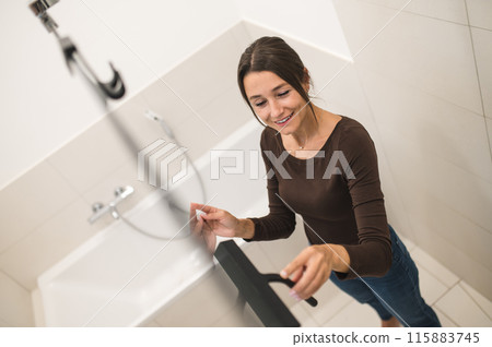 Dark-haired woman cleaning the shower cabin and looking contented Dark-haired woman cleaning the shower cabin and looking contented 115883745