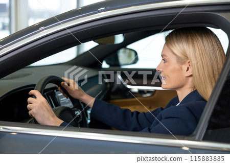 Confident blonde woman sitting in a car and looking determined Confident blonde woman sitting in a car and looking determined 115883885