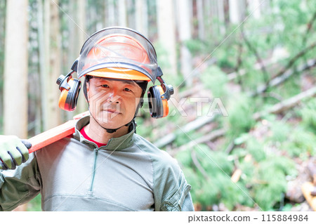 Forest worker facing forward with covered chainsaw on shoulder 115884984
