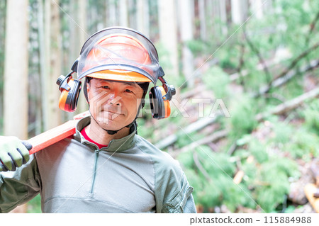 Forest worker facing forward with covered chainsaw on shoulder 115884988