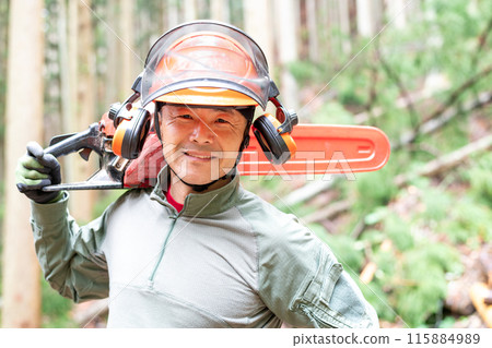 A forest worker smiling and facing forward with a covered chainsaw on his shoulder 115884989