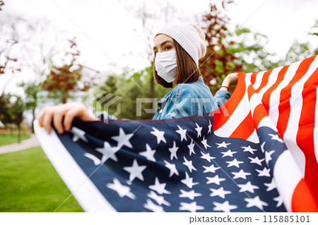 Girl in protective sterile medical mask and with american flag in hand. Quarantine city. Covid -19. 115885101