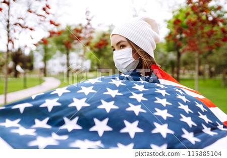 Girl in protective sterile medical mask and with american flag in hand. Quarantine city. Covid -19. Girl in protective sterile medical mask and with american flag in hand. Quarantine city. Covid -19. 115885104