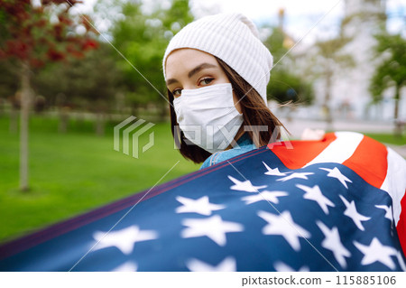 Girl in protective sterile medical mask and with american flag in hand. Quarantine city. Covid -19. 115885106