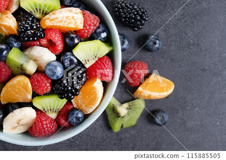 Fruit salad in a blue bowl on black background Fruit salad in a blue bowl on black background 115885505