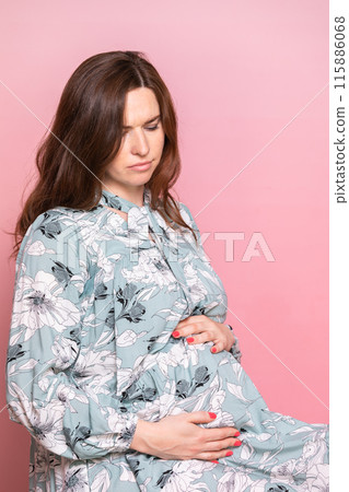 Thoughtful Pregnant Woman in Floral Dress Holding Belly 115886068