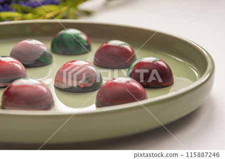 Collectible handmade tempered chocolate candies with a glossy painted body on a round plate with a blurred background and bokeh elements 115887246