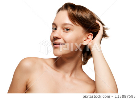 Naturally, fresh looking woman with short brown hair smiles playfully, running her hand through her hair against white studio background. 115887593