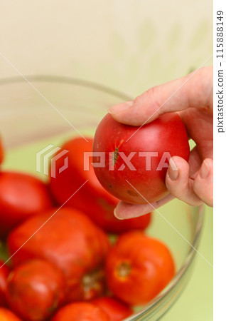 A female hand takes a ripe delicious tomato from a glass bowl. 115888149