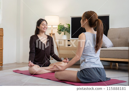 Lesbian Couple Practicing Yoga Together at Home, Engaged in Stretching and Meditation, Promoting Health and Wellness in a Modern Living Room Setting 115888181