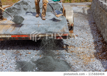 Workers fill parking lot near house with small stones during leveling of driveway Workers fill parking lot near house with small stones during leveling of driveway 115888404