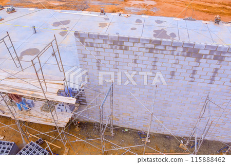Bricklayers build concrete walls using concrete blocks while standing on scaffolds 115888462