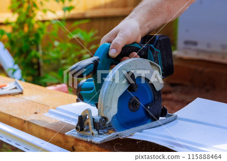 As part of construction of facade of craftsman, he cuts the vinyl siding panel to desired size before it is installed As part of construction of facade of craftsman, he cuts the vinyl siding panel to desired size before it is installed 115888464