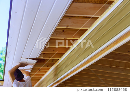 Plastic soffit boards are mounted to roof rafters of house ceiling 115888468