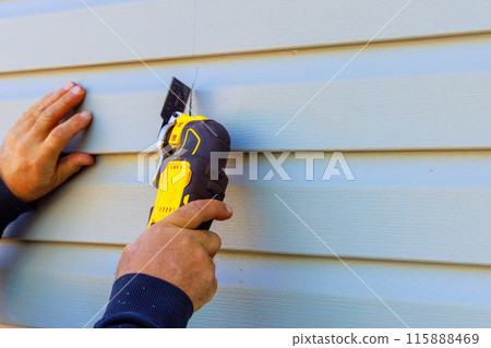 Damaged vinyl siding of house was removed using multi tool during reconstruction Damaged vinyl siding of house was removed using multi tool during reconstruction 115888469