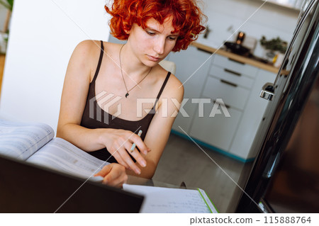 portrait red-haired teenage girl sitting at table in room using computer portrait red-haired teenage girl sitting at table in room using computer 115888764