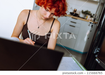 portrait red-haired teenage girl sitting at table in room using computer portrait red-haired teenage girl sitting at table in room using computer 115888765
